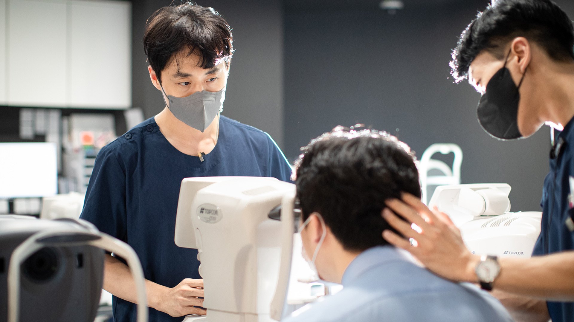 검사 장비 앞에 앉은 환자의 눈을 함께 확인하는 의료진 두 명